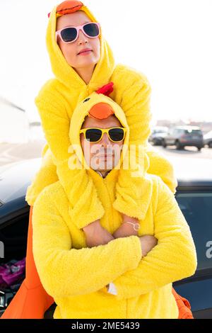 Amici in occhiali da sole e costumi di pollo gialli davanti all'auto Foto Stock