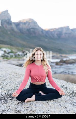 Giovane donna sorridente meditando sulla roccia Foto Stock