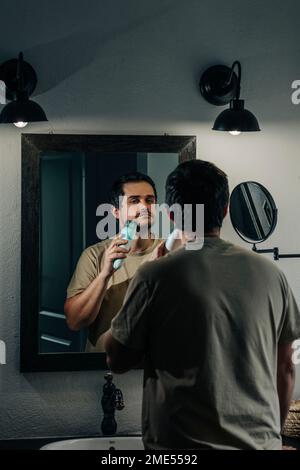 Uomo che si rade con rasoio elettrico in bagno Foto Stock
