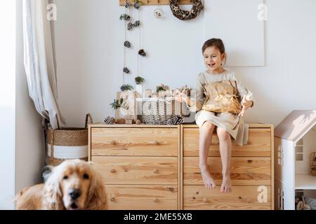Ragazza felice guardando il cane e gesturing davanti al muro Foto Stock