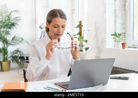 Donna d'affari matura che indossa occhiali seduti in ufficio Foto Stock