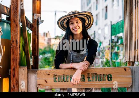 Felice giovane donna in piedi dietro cartello in giardino urbano Foto Stock