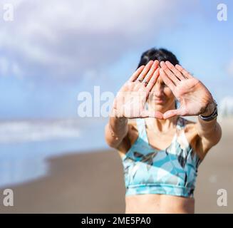 Ripresa ritagliata di una donna irriconoscibile che fa il triangolo mudra in spiaggia Foto Stock