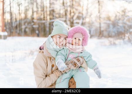 Ritratto di una ragazza carina e ruddy bambino in una calda mint-colorato downy complessivo con pelliccia rosa, insieme con sua madre, una giovane donna bianca in un Foto Stock