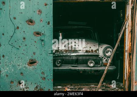 Auto d'epoca rotta è nel garage. Sul corpo della vettura ci sono buchi da proiettili e shrapnel. Guerra in Ucraina. Invasione russa dell'Ucraina Foto Stock