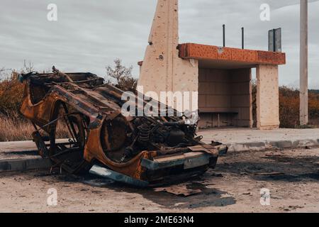 Campagna. Un'auto civile bruciata rovesciata si trova alla stazione degli autobus. Guerra in Ucraina. Invasione russa dell'Ucraina. Crimini di guerra Foto Stock