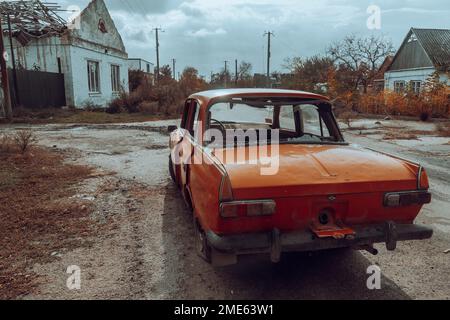 Auto civile danneggiata si trova vicino a una casa distrutta. Il corpo della vettura presenta fori da proiettili e schegge. Guerra in Ucraina. Invasione russa dell'Ucraina Foto Stock