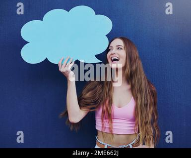 Donna felice che tiene una bolla di discorso con lo spazio mockup in piedi da una parete blu con un segno. Gen z, felicità e giovane donna con una chat board con Foto Stock