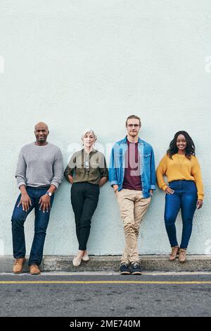 Il mondo saprà tutto su di noi abbastanza presto. Foto a tutta lunghezza di un gruppo di uomini d'affari in piedi in linea contro un muro all'aperto. Foto Stock