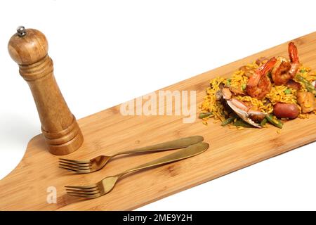 Riso paella servito su un asse di legno con shaker di sale e forchette preparate con frutti di mare, amaroni, zafferano, salsiccia, carne. Piatto tradizionale di Valenci Foto Stock