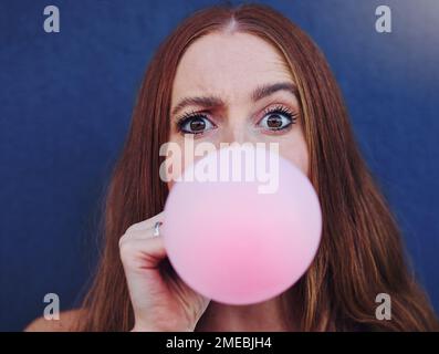 Primo piano ritratto, ragazza e bubblegum a parete, all'aperto e avventura urbana per divertente, comico volto e felice. Gen z donna, città e sfondo blu con Foto Stock