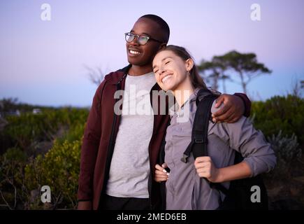 Coppia, avventura e rapporto interrazziale durante il tramonto di sera o di notte all'aperto in natura. Amore, viaggi e persone che abbraccia all'aperto Foto Stock
