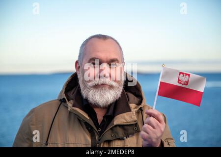 Uomo con bandiera polacca. Ritratto dell'uomo anziano con bandiera nazionale polacca. Visita il concetto di Polonia. Uomo anziano di 55 60 anni che viaggia in inverno Foto Stock