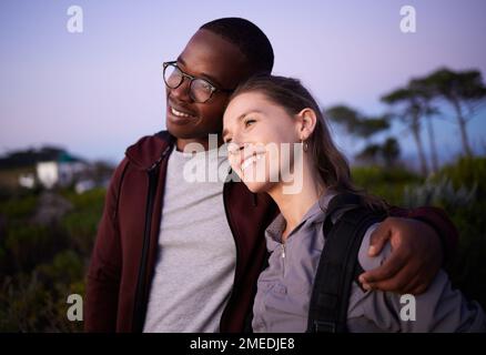 Coppia felice, relax e amore in un rapporto interracial durante il tramonto di sera o di notte all'aperto in natura. Avventura, viaggi e persone Foto Stock