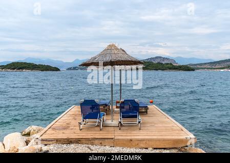 Quattro lettini vuoti sotto gli ombrelloni in riva al mare in condizioni di clima nuvoloso in Albania Foto Stock