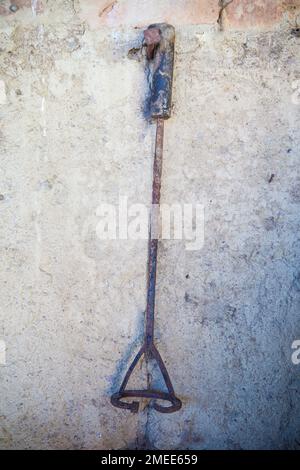 Marcare a caldo ferro per bestiame bovino appeso da un chiodo sulla parete di adobe di una vecchia stalla. Messa a fuoco selettiva Foto Stock