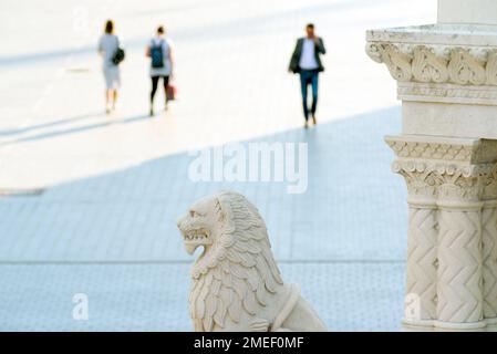 Persone sfocate che camminano contro il monumento curvato in pietra della città Foto Stock