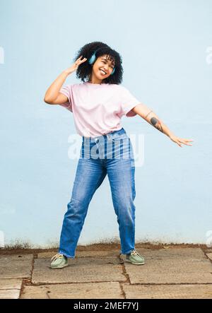 Donna nera, musica e danza con cuffie su sfondo parete all'aperto con energia, libertà e felicità. Ragazza felice ballando alla radio, podcast e. Foto Stock