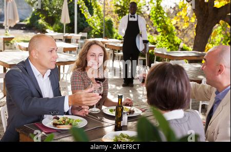Cameriere che serve pasti al cordiale compagnia presso il ristorante all'aperto Foto Stock