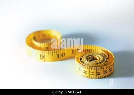 Metro a nastro giallo arrotolato in spirali, strumento di cucito o simbolo per la dieta dimagrante, sfondo grigio chiaro blu con spazio di copia, fuoco selezionato, narro Foto Stock