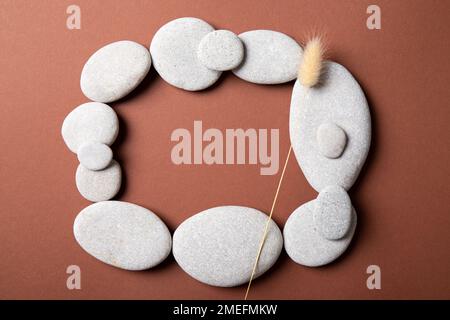 Vista piatta della cornice realizzata con pietre piatte e lisce di mare su fondo marrone vuoto, molto spazio di copia, studio shot. Prodotti biologici minimalisti. Foto Stock