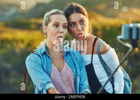 Indovinate chi ha il tempo migliore. due belle amiche che prendono un selfie utilizzando un selfie stick in natura. Foto Stock