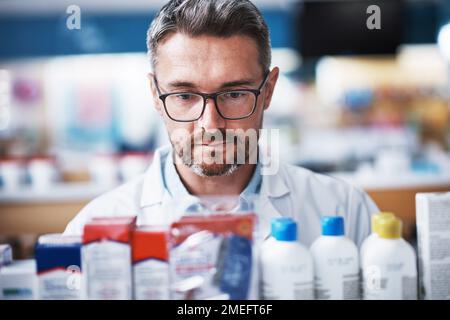 Mantenendo tutti i suoi stock pieni. un farmacista maturo che controlla i prodotti in una farmacia. Foto Stock