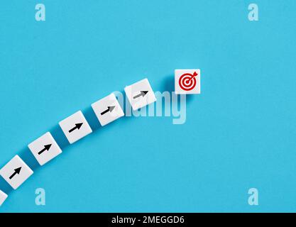 Raggiungimento degli obiettivi e pianificazione strategica del business. Verso gli obiettivi. Simboli freccia e obiettivo su blocchi bianchi su sfondo blu. Foto Stock