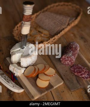 Un cestino con cracker, due tipi di formaggio e salumi su un tavolo di legno Foto Stock