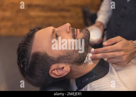 Barbiere che applica la schiuma sul collo del cliente prima della rasatura Foto Stock