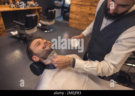 Barbiere che applica la schiuma sul collo del cliente prima della rasatura Foto Stock