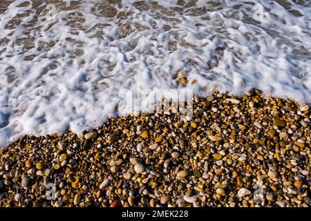 Pietre colorate e spray sulla spiaggia di Capo Bianco. Foto Stock