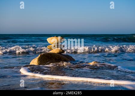 Un gallo di roccia, onde e spray sulla spiaggia di Capo Bianco. Foto Stock