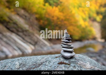 Stack di pietra con pietre equilibrate su sfondo di montagna sfocato al tramonto luce calda nel fogliame autunnale Foto Stock