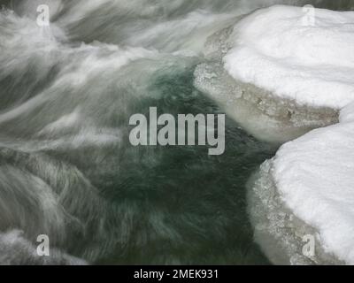 Fiume invernale ghiacciato con neve e ghiaccio sulla riva, movimento dell'acqua in esposizione lunga Foto Stock