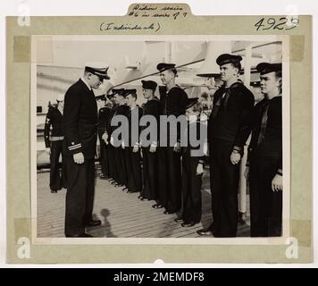 Il ragazzo di mistero del fronte d'acqua tedesco (No. 6 in Una serie di 7 foto). Momento critico - ispezione prima di andare a riva per la libertà di una serata. Se non si passa questo, ragazzo, si rimane a bordo! Tuttavia, se Eddie piazza il suo cappello, probabilmente passerà muster o.k. Lieut. Frederick A. Goettel, di New London, Connecticut, che è grande quanto Eddie è piccolo, dà al ragazzo il vecchio occhio di gimlet che fa sì che i Coast Guardsmen scendono a terra in un'attrezzatura adeguata e in forma di nave. Lieut. Goettel, che a proposito è sei piedi quattro, e pesa 230 libbre, è uno degli ufficiali attaccati al Coast Guard Cutter EAGLE, di Foto Stock