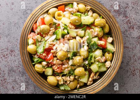 Insalata di olive verdi turche con noci, pomodori, cetrioli, prezzemolo primo piano in un piatto sul tavolo. Vista orizzontale dall'alto Foto Stock