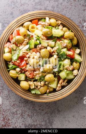 Insalata vegetariana di olive verdi con noci, pomodori, cetrioli conditi con melassa melograna primo piano in un piatto sul tavolo. Vista verticale dall'alto Foto Stock