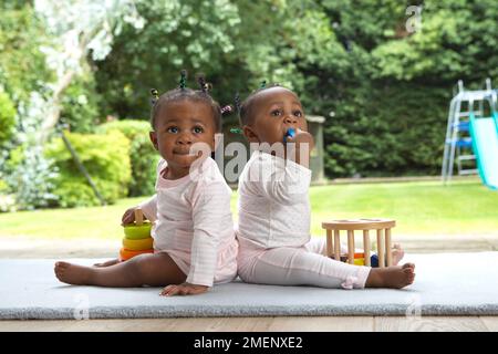 Due bambine che siedono insieme sul tappetino, vista laterale, 9 mesi Foto Stock