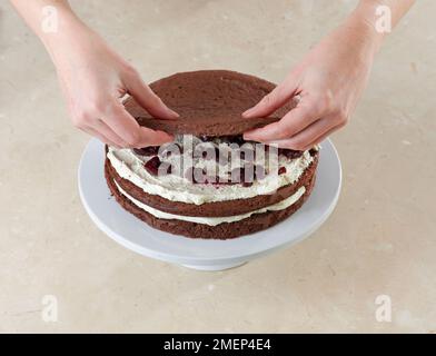 Black Forest Gateau, schiacciando lo strato finale di spugna su panna montata e ciliegie Foto Stock