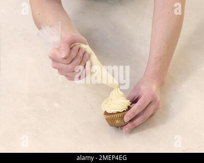 Crema alla vaniglia Cupcakes, infilando una spirale di glassa sulla torta Foto Stock