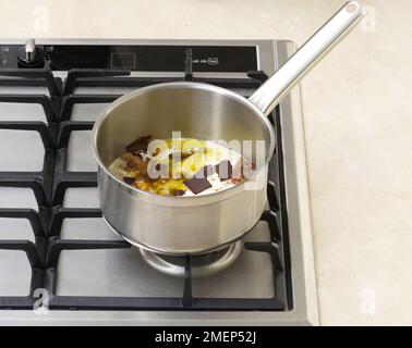 Preparazione di Profiteroles, aggiunta di cioccolato, burro e sciroppo alla crema in padella e riscaldamento fino a fusione Foto Stock