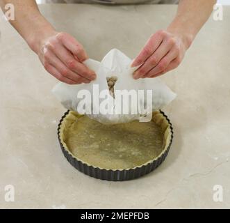 Rimuovere i fagioli e la carta da forno dalla base per pasticceria, facendo una crostata Foto Stock