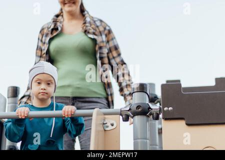 Ragazzino con sindrome di Down che scende giù per la collina. Mamma sullo sfondo Foto Stock