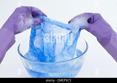 Sciacquare il tessuto di seta in una ciotola di acqua calda per rimuovere eventuali residui di colore e sale, primo piano Foto Stock