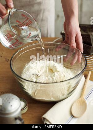 Versando acqua dalla caraffa da miscelare con altri ingredienti nella ciotola (produzione di pane) Foto Stock