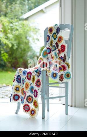 Coperta a crochet colorata con motivo floreale drappeggiata sulla sedia Foto Stock