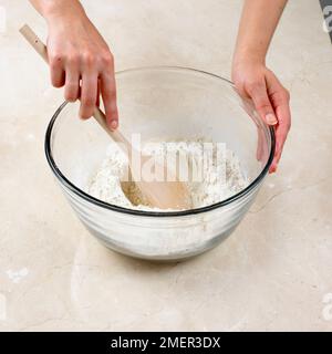 Preparare la pasta di crosta in acqua calda, utilizzando un cucchiaio per ottenere un composto ben al centro della farina Foto Stock