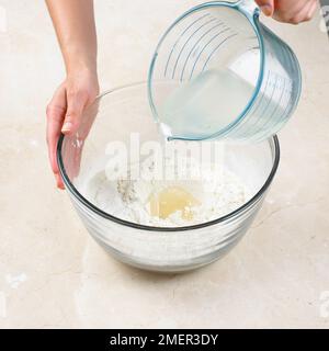 Rendendo in acqua calda pasta frolla, versando acqua calda grasso fuso miscela in bene nel centro della miscela di farina Foto Stock