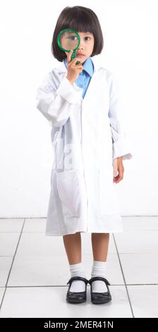 Ragazza in camice da laboratorio, mano sul mento, guardando in alto, 6 anni Foto Stock